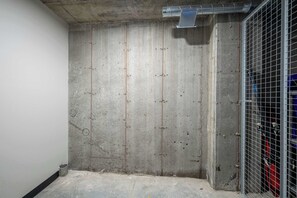 Canteiro de obras com paredes de concreto aparente, porta de metal e chão de concreto.