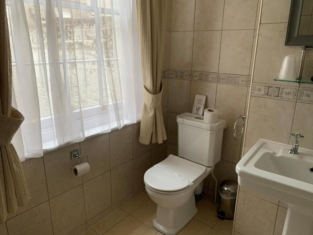 Un bagno con WC, lavandino e finestra con tende.