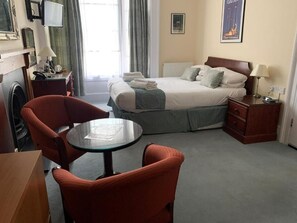 Een hotelkamer met een bed, een ronde tafel, twee stoelen, een bureau, een lamp, een televisie en een radiator.