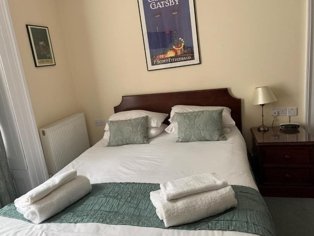 Een hotelkamer met een netjes opgemaakt bed, een poster aan de muur en een nachtkastje met een lamp.
