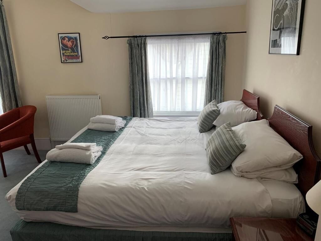 A hotel room with a large bed, a chair, a radiator, and a window with curtains.