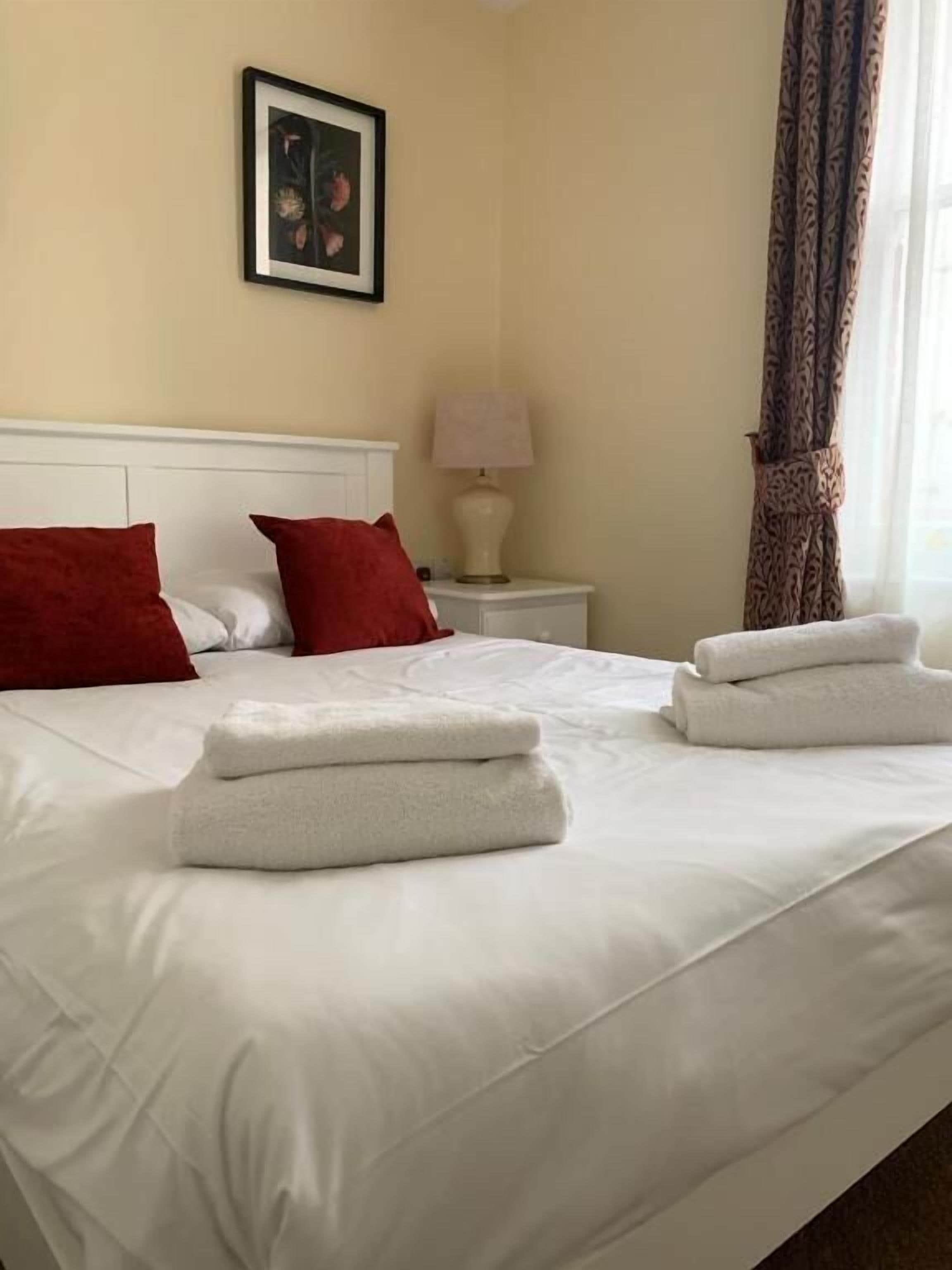 A hotel room with a bed, pillows, a nightstand with a lamp, and a framed picture on the wall.