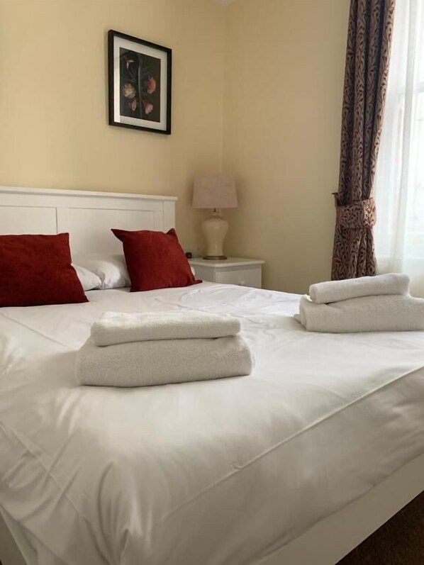 Una habitación de hotel con cama, almohadas, mesita de noche con lámpara y un cuadro en la pared.