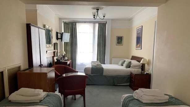 A hotel room with two beds, a desk, a chair, a television, and a window with curtains. - Peregrine House  (Canterbury)