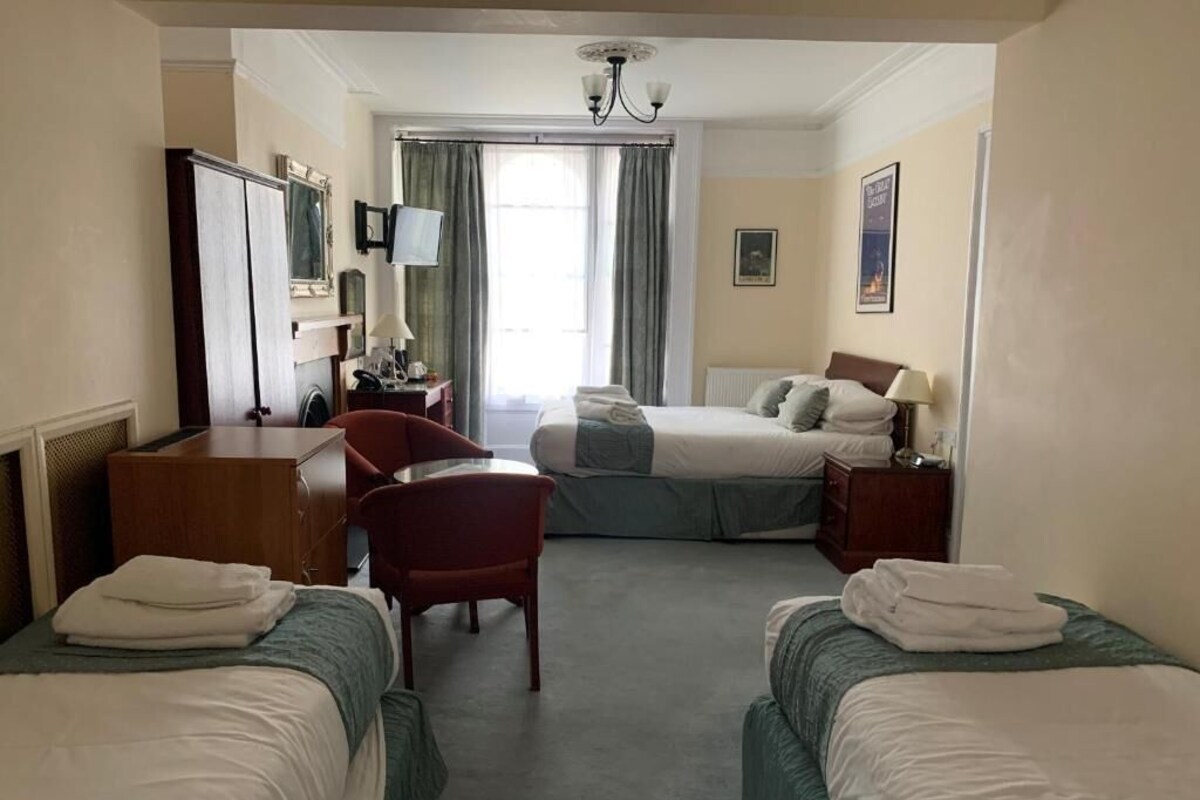 Een hotelkamer met twee bedden, een bureau, een stoel, een televisie en een raam met gordijnen.