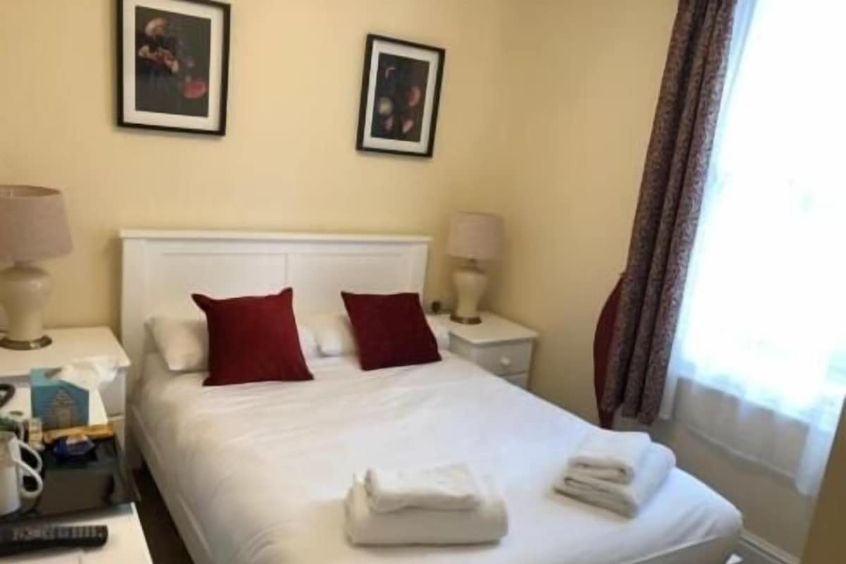 Een hotelkamer met een bed, twee nachtkastjes, een lamp en een raam met gordijnen.