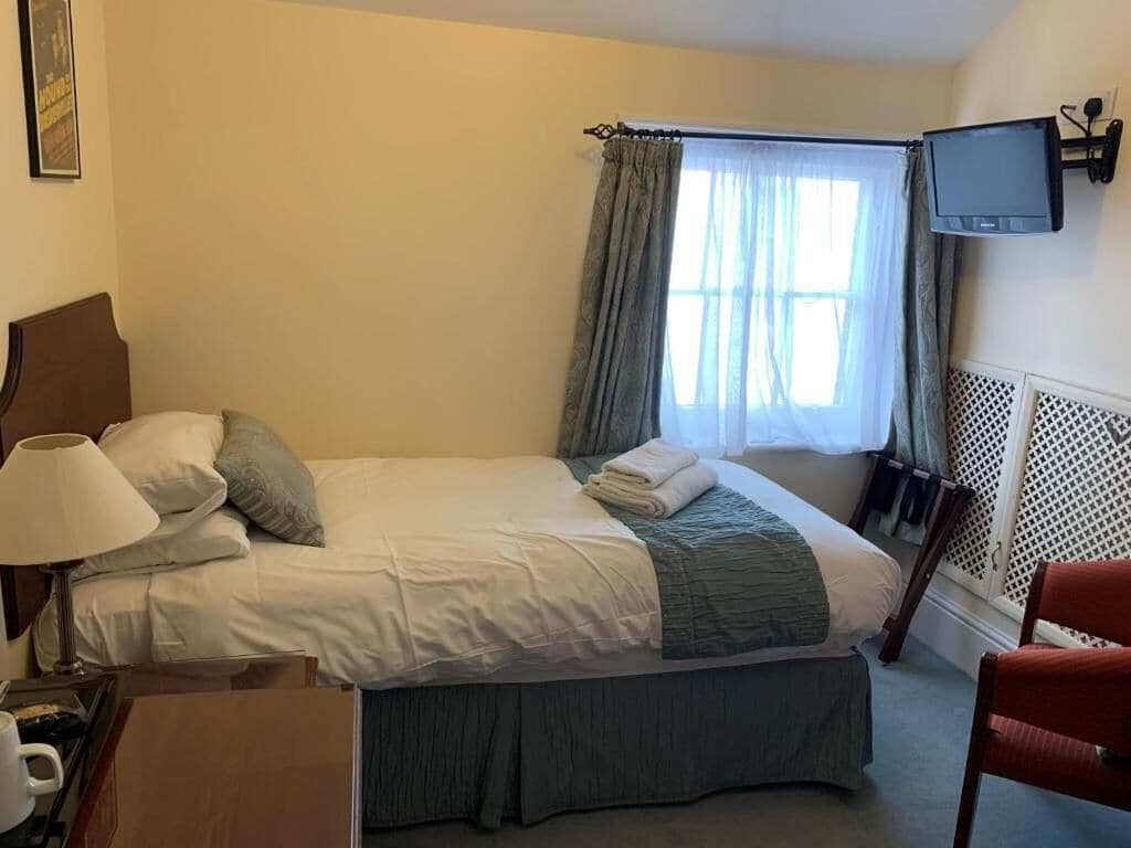 Une chambre d’hôtel avec un lit, un téléviseur fixé au mur, une fenêtre avec des rideaux et une chaise.