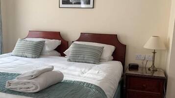 Una cama bien hecha con almohadas y toallas dobladas, una mesita de noche con lámpara y un cuadro en la pared.