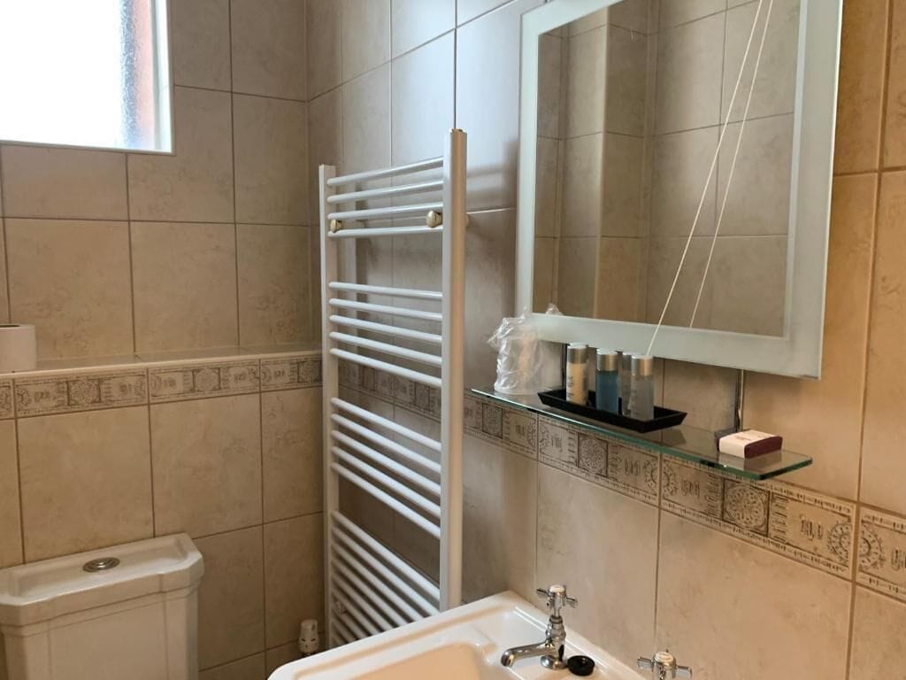 Une salle de bain avec un lavabo blanc, un miroir, un porte-serviettes et une étagère en verre où sont rangés les articles de toilette.