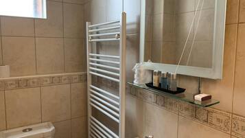 Une salle de bain avec un lavabo blanc, un miroir, un porte-serviettes et une étagère en verre où sont rangés les articles de toilette.