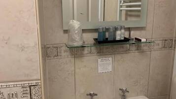 Une salle de bain avec un lavabo blanc, deux robinets, une étagère en verre où sont rangés les articles de toilette, et un miroir au-dessus du lavabo.