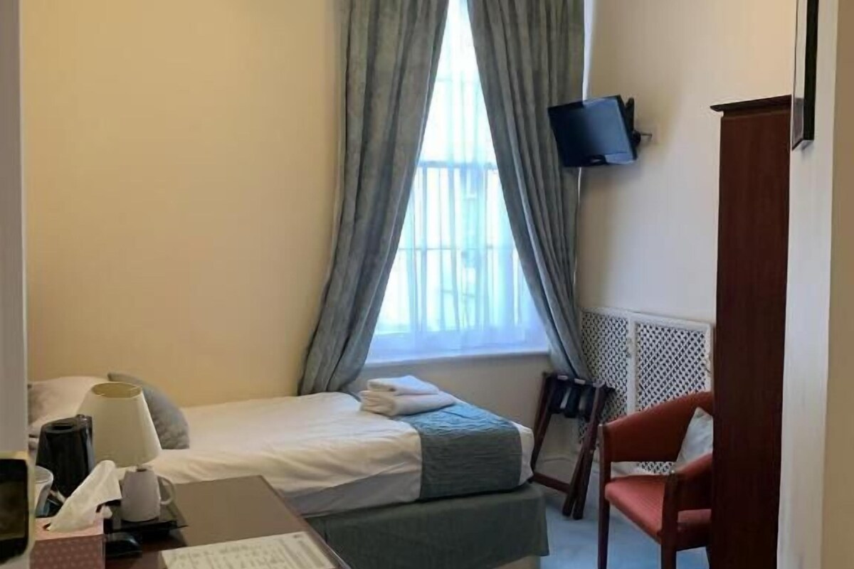 Een hotelkamer met een bed, bureau, stoel en een televisie aan de muur.
