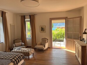 A room with a bed, two armchairs, a wooden cabinet, and a large window with a view of greenery. - Exclusive villa on Lake Attersee, right on the shore, with a boathouse featuring a seating area and a dock (Unterach am Attersee)