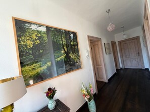 A hallway with a large framed forest photograph, two vases with flowers, and a wooden door. - Exclusive villa on Lake Attersee, right on the shore, with a boathouse featuring a seating area and a dock (Unterach am Attersee)