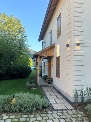 A two-story building with a wooden porch, stone pathway, and a well-maintained garden. - Exclusive villa on Lake Attersee, right on the shore, with a boathouse featuring a seating area and a dock (Unterach am Attersee)