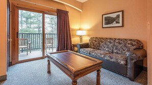 Una habitación con mesa de billar, sofá, sillón, balcón con vistas a árboles y una lámpara.