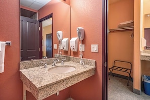 Un baño de hotel con un lavamanos de granito, dos secadores de pelo y un perchero para toallas.