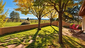 A fenced outdoor area with a lawn, trees, and red chairs. - Vistas de Las Animas - Sweeping Fall Foliage Views (Arroyo Seco)