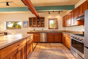 A kitchen with wooden cabinets, a stainless steel dishwasher, a built-in oven, and a window with a view of trees. - Vistas de Las Animas - Sweeping Fall Foliage Views (Arroyo Seco)