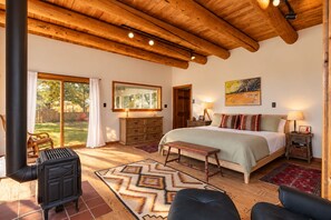 Un dormitorio con una cama grande, vigas de madera en el techo, una chimenea y vistas a través de un ventanal corredero.