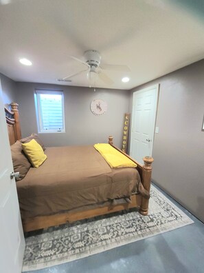 A bedroom with a bed, a ceiling fan, a window with blinds, a door, and a wall clock. - Charming 5-bedroom house fits 12 guests in cozy Cheyenne (Cheyenne)