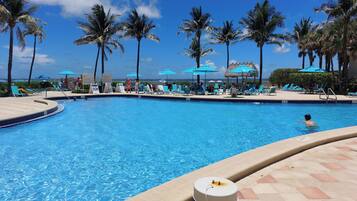 A swimming pool with lounge chairs and umbrellas, surrounded by palm trees.