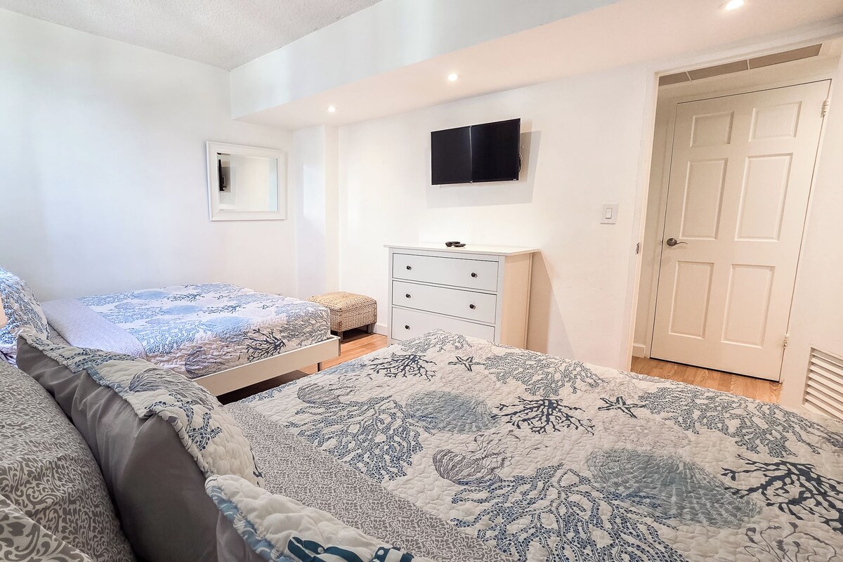 A bedroom with two beds, a dresser, a television, and a door.