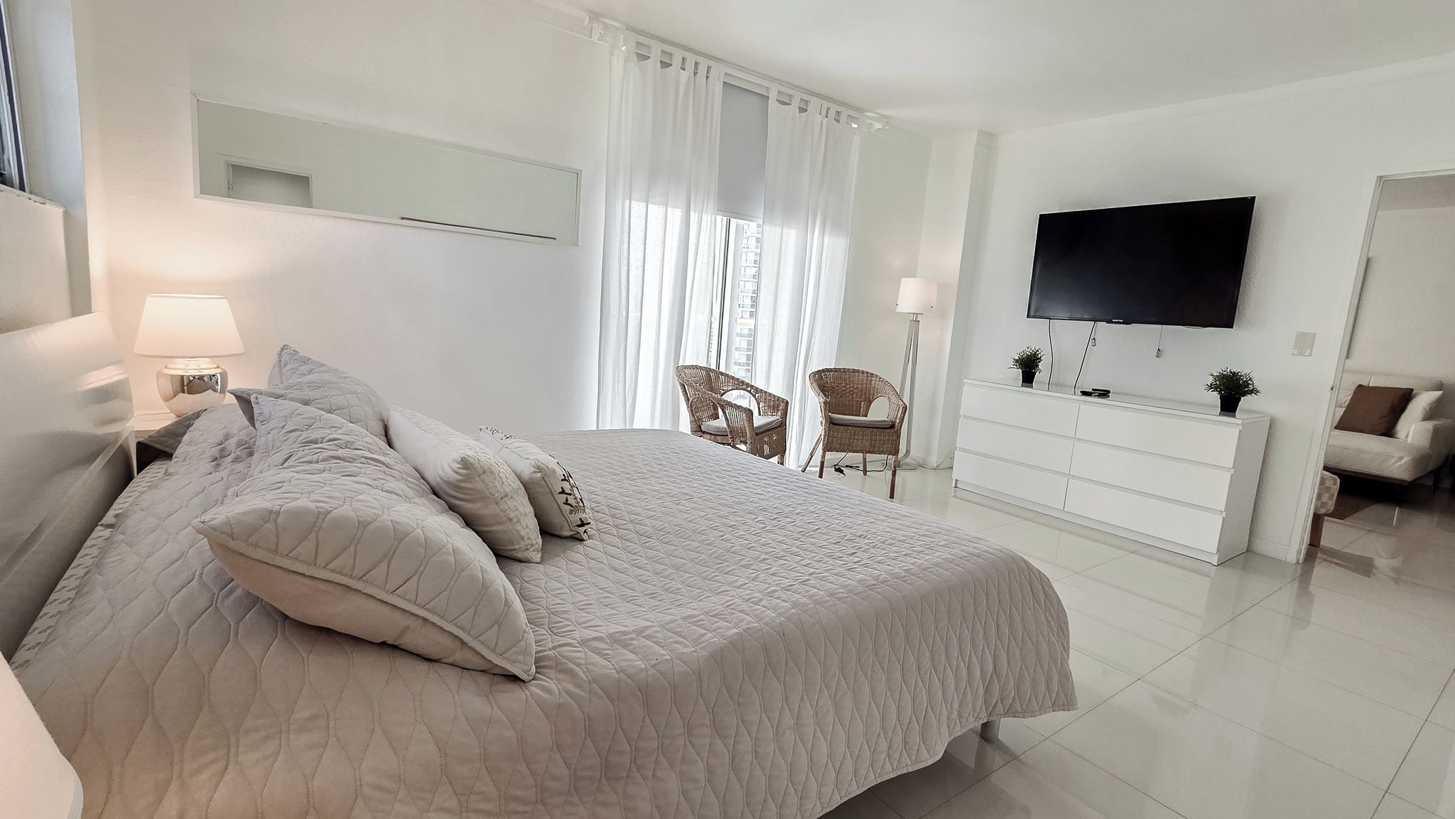 A bedroom with a bed, a dresser, a television, and two chairs.