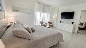 A bedroom with a bed, a dresser, a television, and two chairs.