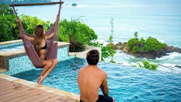 Un espace aménagé au bord de la piscine, avec vue sur l’océan, un hamac et une personne assise près de la piscine.