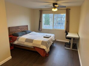 A bedroom with a bed, a desk, a ceiling fan, and a window.