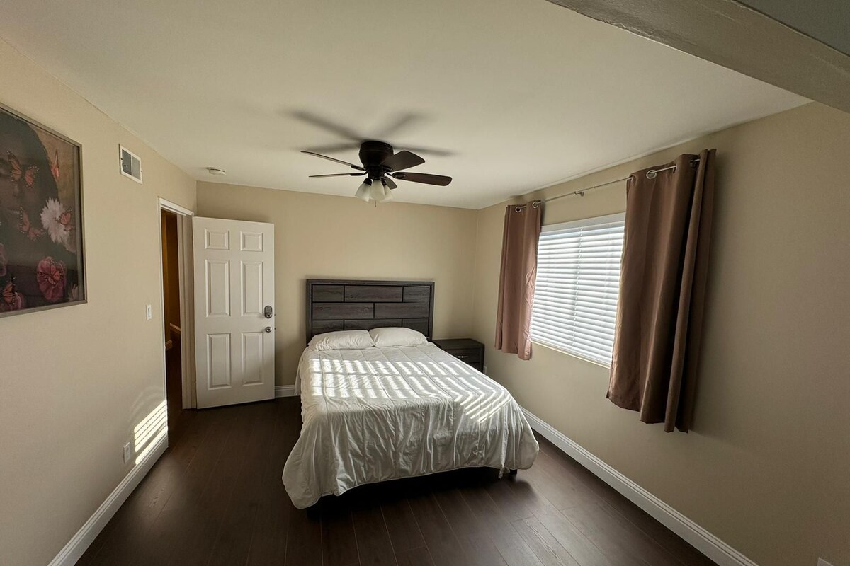 A bedroom with a bed, a ceiling fan, a door, and a window with curtains.