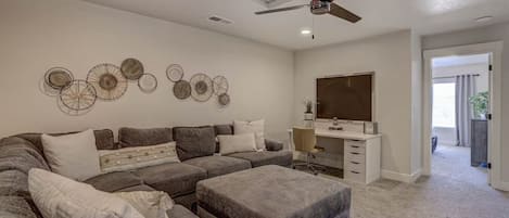 Un salon moderne avec un canapé d’angle, un bureau et un ventilateur de plafond.