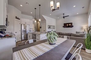 A modern kitchen with stainless steel appliances, a dining area with a striped table runner, and a living area with a sofa and a TV. - Serene Retreat by Zion | Hot Tub • Pool • Fire Pit (Washington)