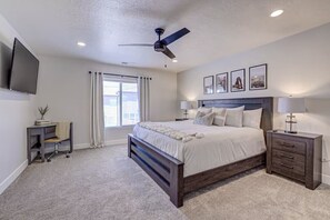 A bedroom with a bed, bedside tables, a desk, a ceiling fan, and a TV mounted on the wall. - Serene Retreat by Zion | Hot Tub • Pool • Fire Pit (Washington)