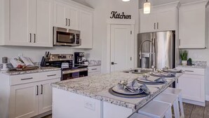 A modern kitchen with white cabinetry, a large island, stainless steel appliances, and pendant lighting.