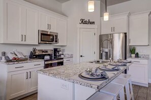 A modern kitchen with white cabinetry, a large island, stainless steel appliances, and pendant lighting.