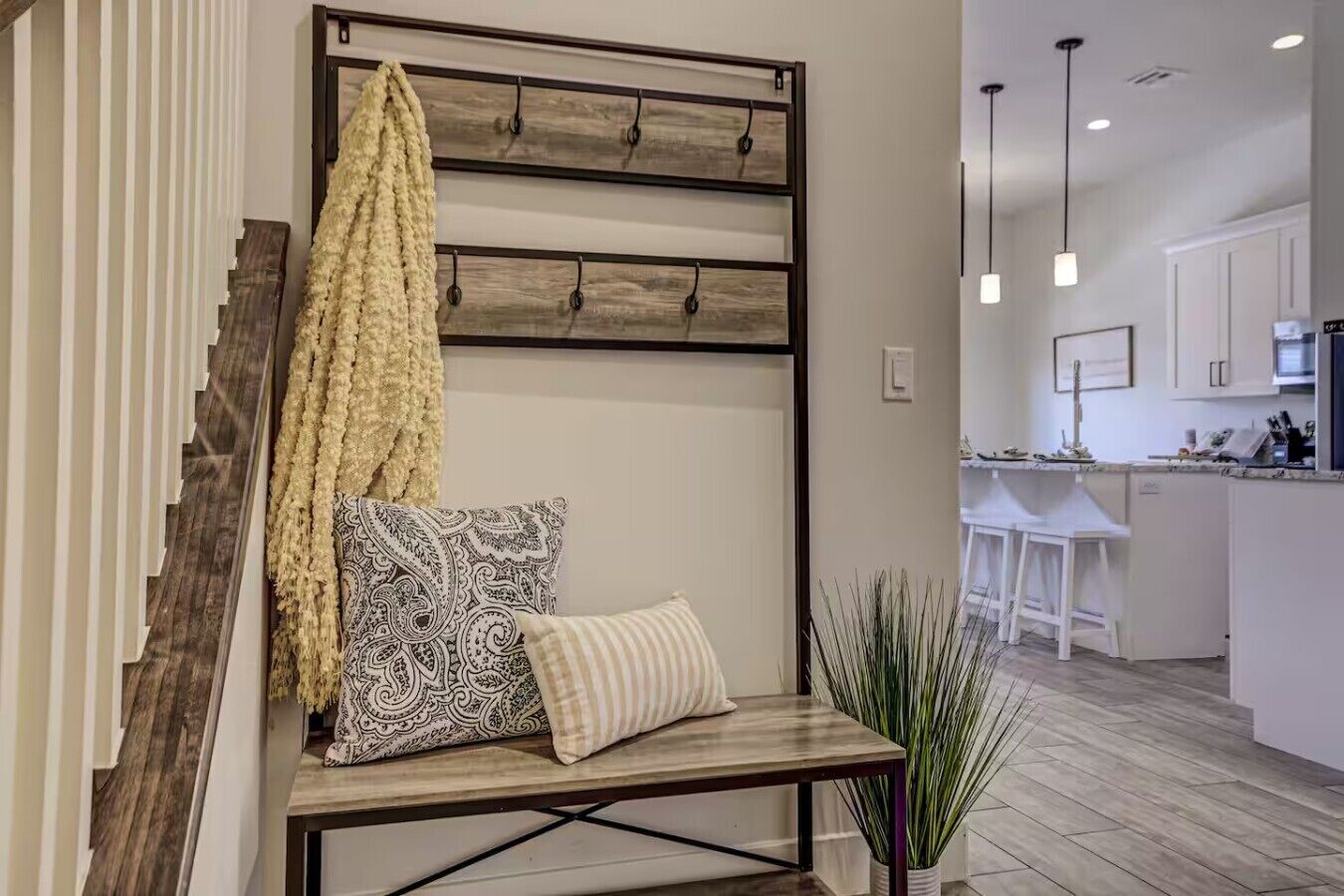 A modern interior with a bench, patterned pillows, a hanging yellow towel, and a kitchen area in the background.