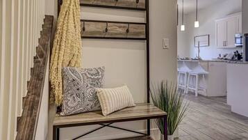 A modern interior with a bench, patterned pillows, a hanging yellow towel, and a kitchen area in the background.