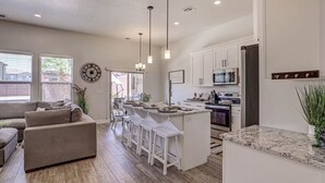 A modern kitchen with white cabinetry, a central island with bar stools, and a dining area with a sofa and chairs.