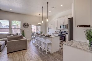 A modern kitchen with white cabinetry, a central island with bar stools, and a dining area with a sofa and chairs.