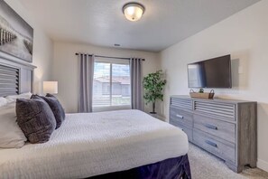A bedroom with a bed, a dresser, a television, and a window with curtains.