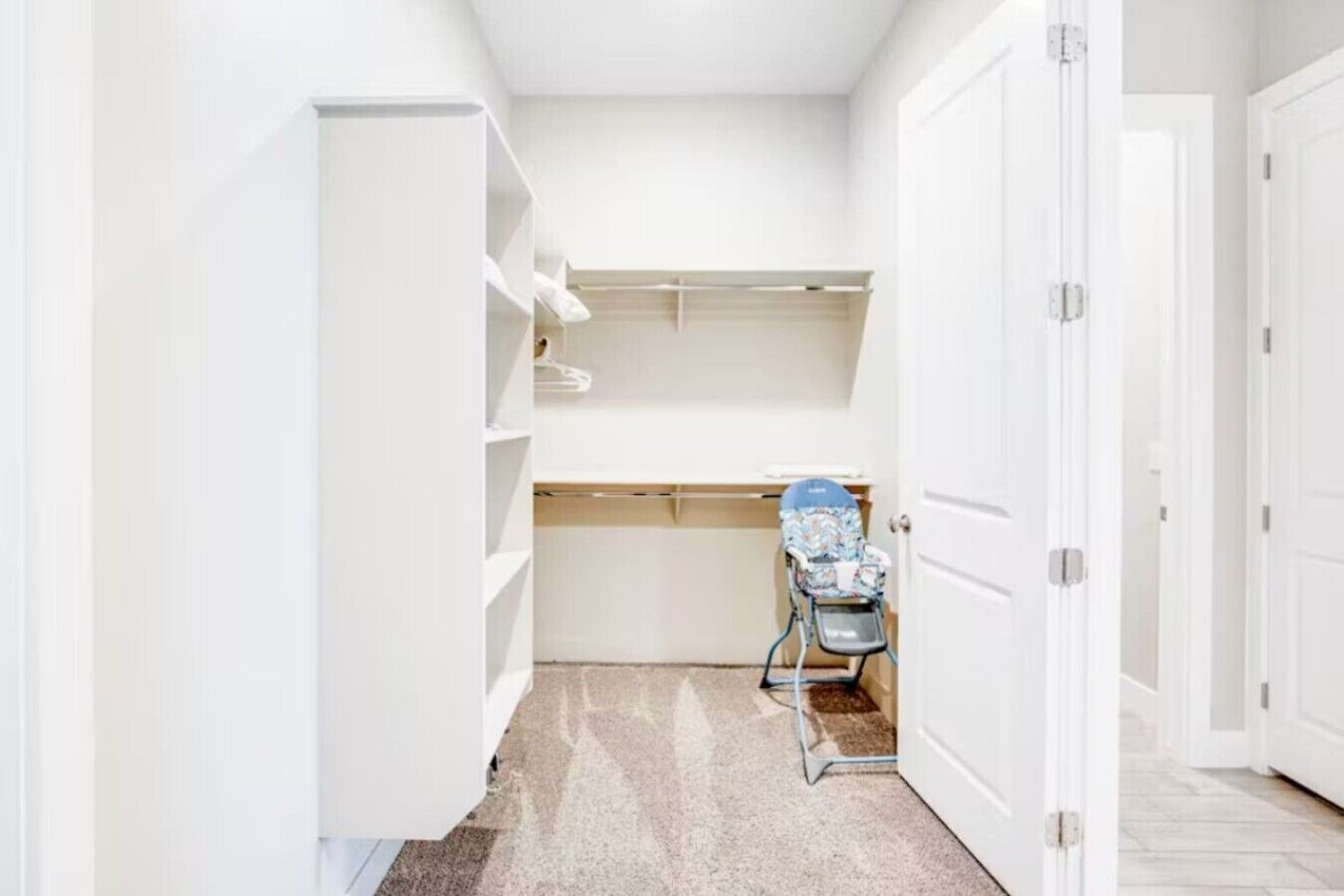 A narrow hallway with white walls, a baby changing station with a stroller, and a door on the right.