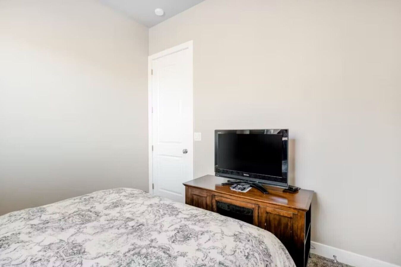 A bedroom with a bed, a television on a wooden dresser, and a white door.