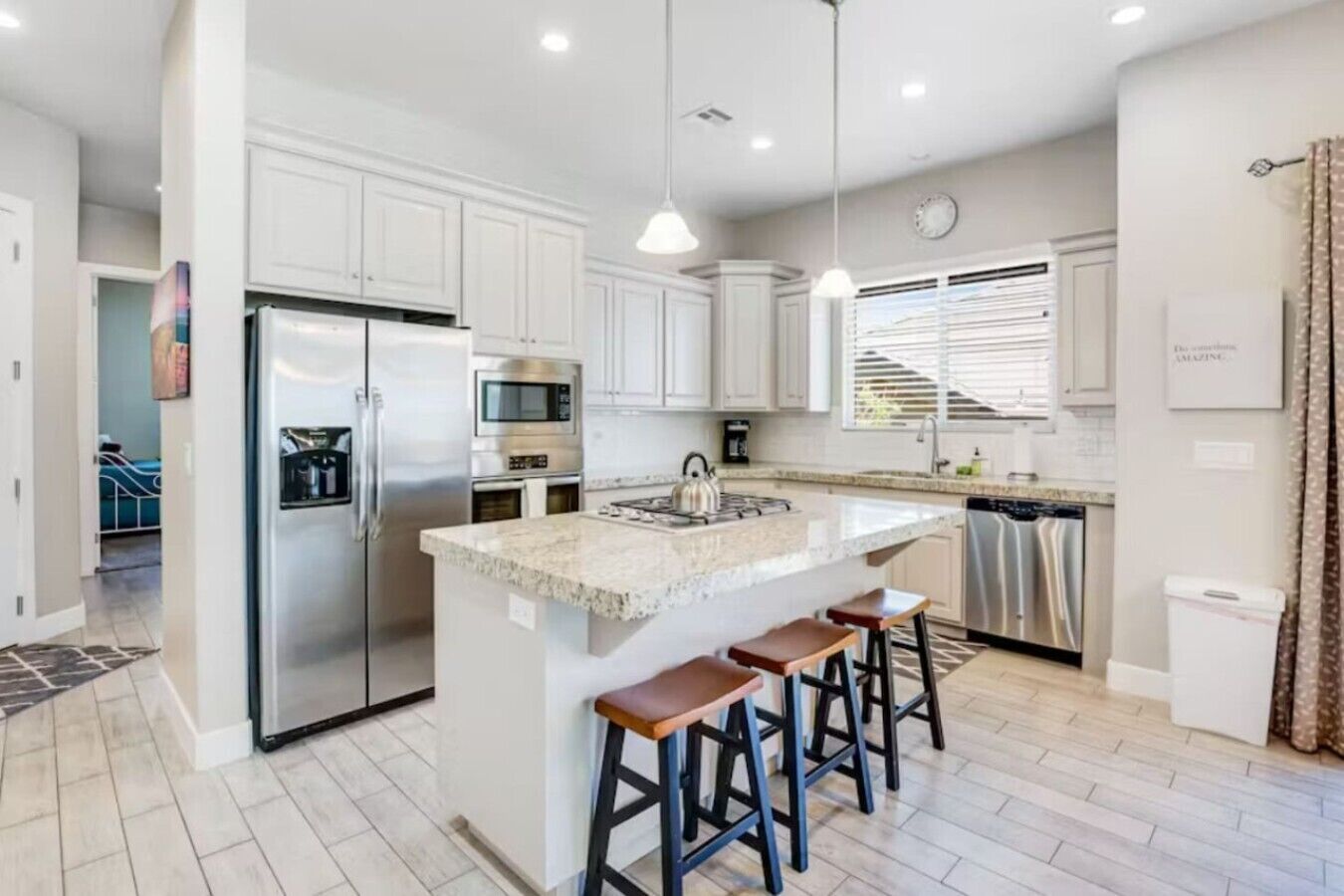 A modern kitchen with white cabinets, stainless steel appliances, a granite countertop, and a bar stool seating area.