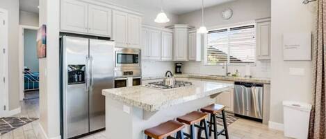 A modern kitchen with white cabinets, stainless steel appliances, a granite countertop, and a bar stool seating area.