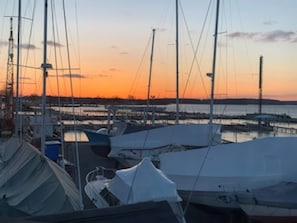 A marina with multiple boats docked, a clear sky, and a distant view of land across the water. - Lakefront Gem | Cozy Stay w/ Dock + Sunset Views (Sodus Point)