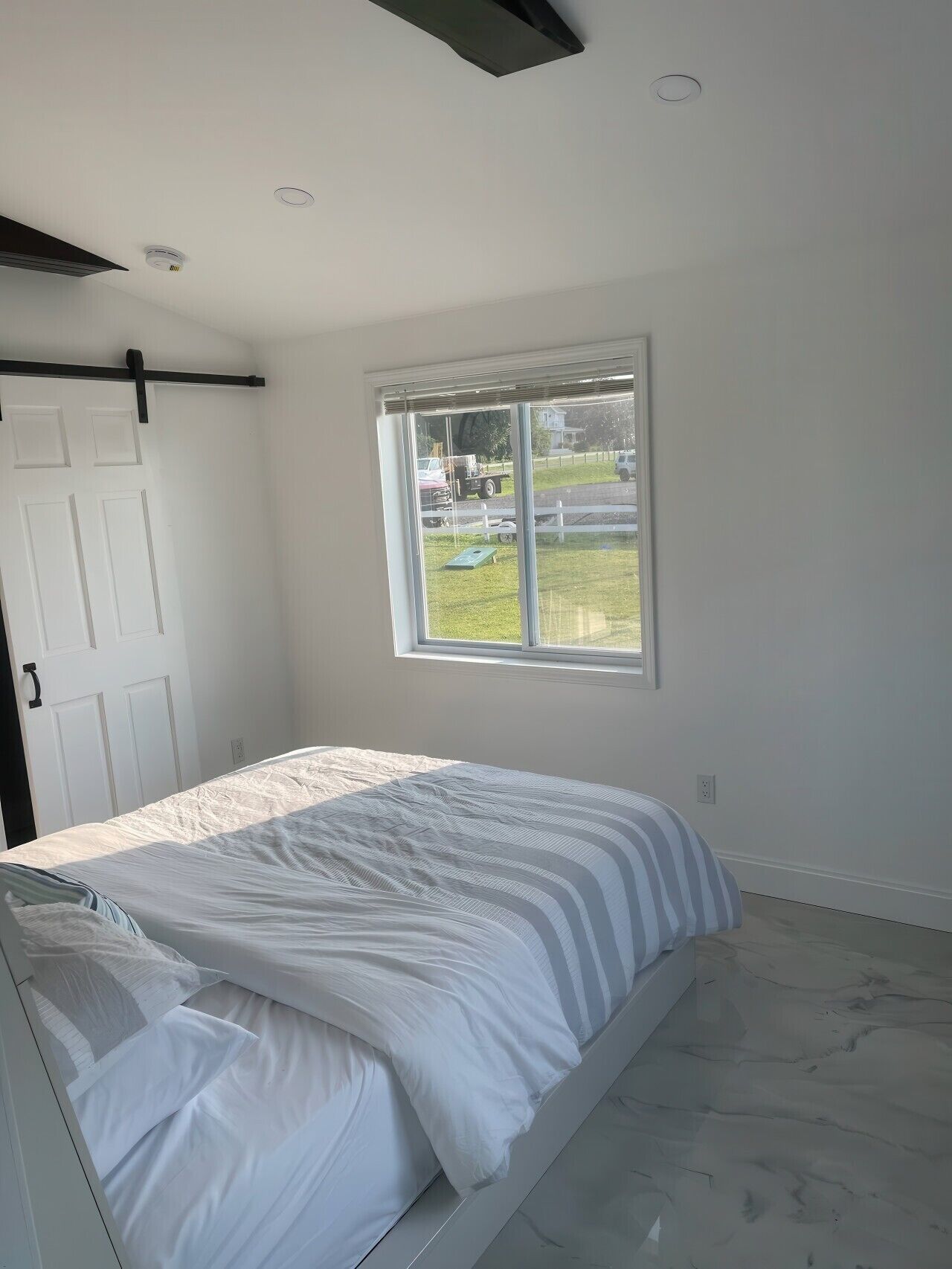 A bedroom with a bed, a window, a door, and a ceiling fan.