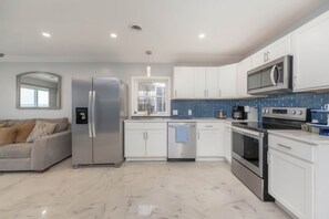 A modern kitchen with white cabinets, stainless steel appliances, and a blue-tiled backsplash. - Lakefront Gem | Cozy Stay w/ Dock + Sunset Views (Sodus Point)