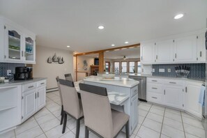 Une cuisine moderne avec des meubles blancs, un îlot central doté de sièges et une vue sur la mer grâce à de grandes fenêtres.